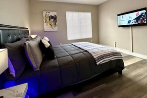 A bedroom with a bed, a television on the wall, and a window with blinds. - Modern 2BR Condo Near the Las Vegas Strip (Las Vegas)