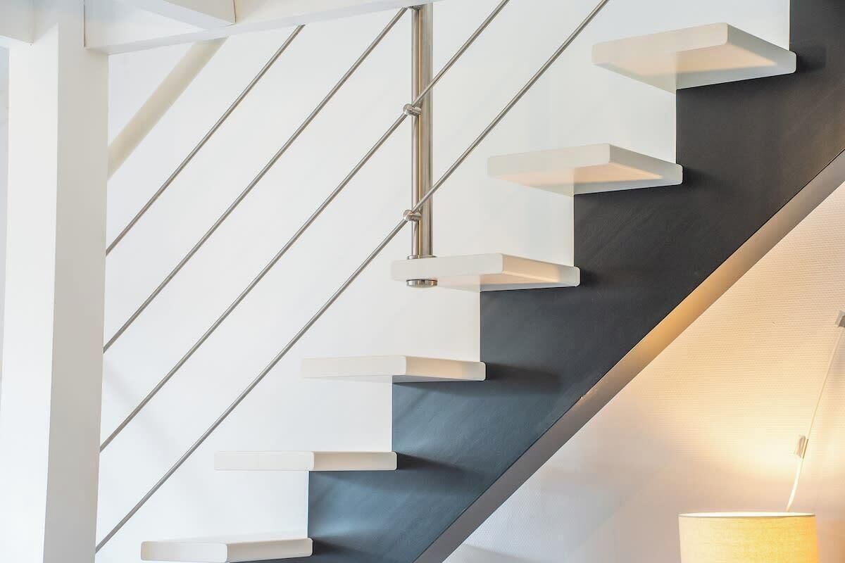 Un escalier moderne avec des marches blanches en porte-à-faux et une rampe en métal, menant à un étage sombre.