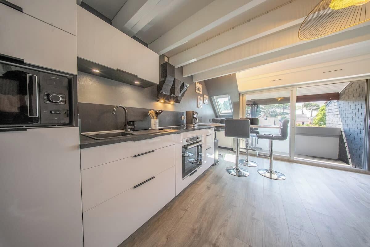Een moderne keuken met witte kasten, een inbouwoven, een magnetron en een eethoek met twee barkrukken.