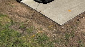 Un barbecue extérieur abrité, attenant à un garage doté d’un plancher en béton et d’une clôture en métal.
