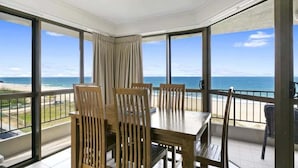 Ein Balkon mit Tisch und Stühlen, Blick auf den Strand und einen klaren Himmel.