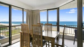 Ein Balkon mit Tisch und Stühlen, Blick auf den Strand und einen klaren Himmel.
