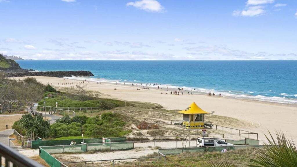 A beach with a yellow pavilion, a sandy shore, and a clear blue sky.