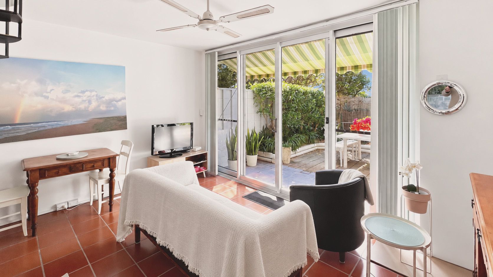 A room with a bed, a TV, a desk, and a view of the outdoors through a sliding glass door.