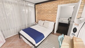 Une chambre à coucher avec un lit, une table de chevet, une lampe et une vue sur la salle de bain par une porte ouverte.