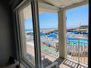 Un balcón con vistas a una zona de piscina, que incluye piscina, sillas de descanso y sombrillas.