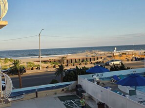 A beachfront view with a pool area, lounge chairs, and a wooden walkway leading to the beach. - Beachfront location, steps from the boardwalk, Fri night fireworks & more! (North Wildwood)