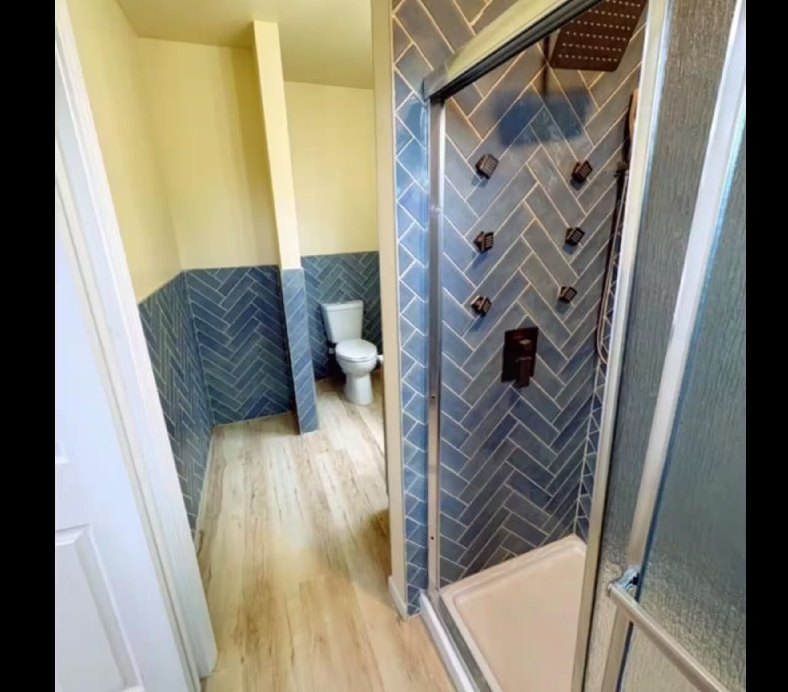 A bathroom with a herringbone-patterned wall, a toilet, and a shower area.