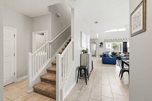 A spacious living area with a staircase, a dining table, and a blue sofa. - Renovated 5BR Pool Home · Game Room · 15 Min to Disney · Sleeps 10 (Four Corners)