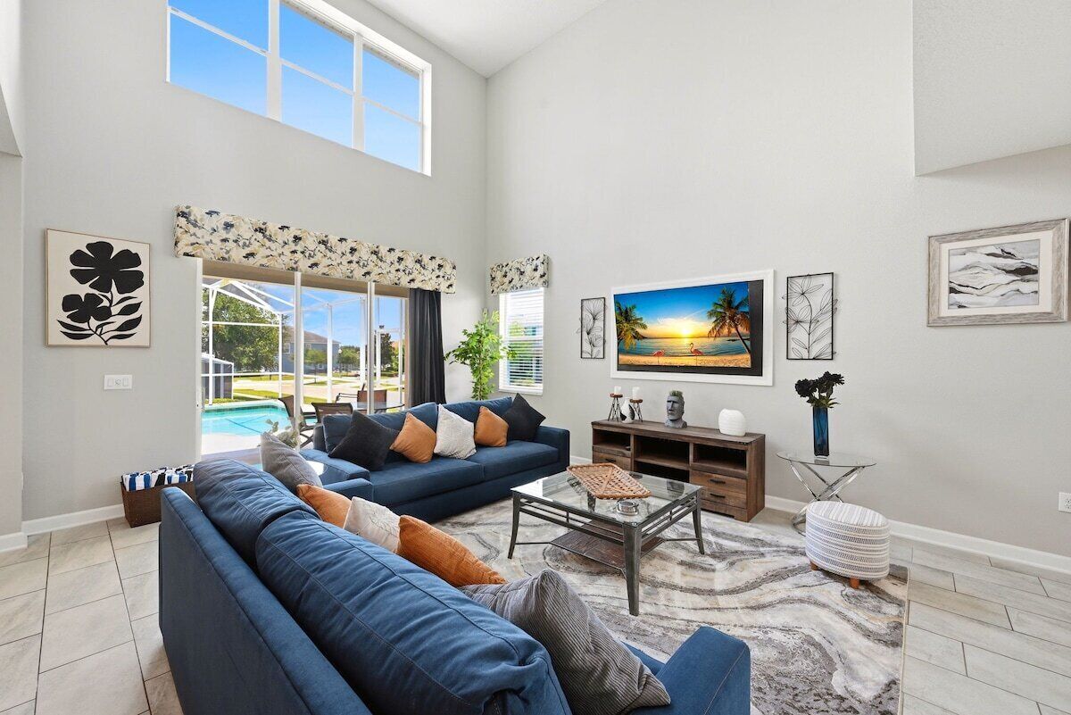 A spacious living room with a large blue sofa, a coffee table, and a painting of a sunset.