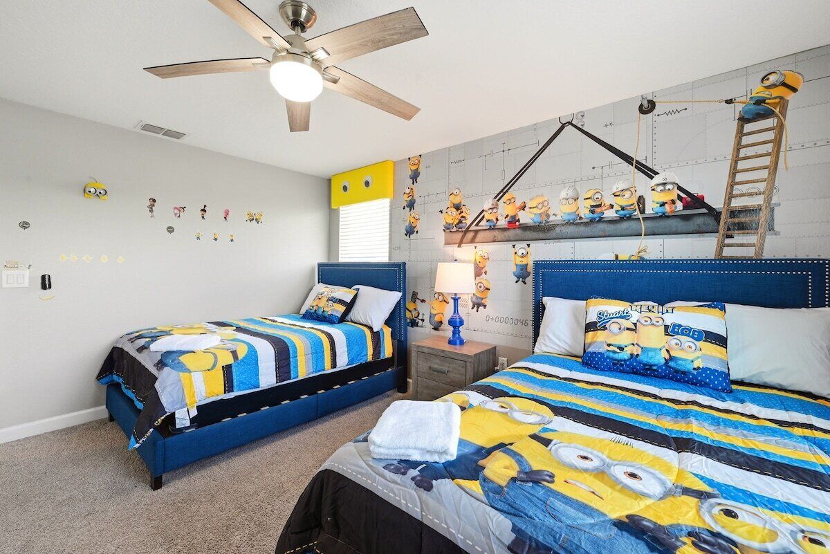Un dormitorio con dos camas, un ventilador de techo y una pared decorada con motivos de minions.