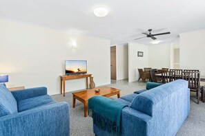 Ein Wohnzimmer mit Fernseher, blauen Sofas, einem Holztisch und einem Deckenventilator.