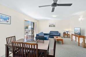 Ein Wohnzimmer mit Esstisch, Stühlen, einer Couch, einem Fernseher und einem Deckenventilator.