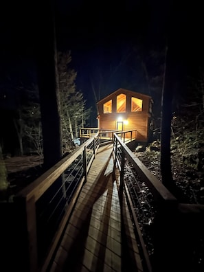 A wooden cabin with a deck leading to the entrance, surrounded by trees.
