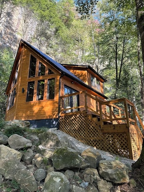 Uma cabana de madeira com telhado inclinado, janelas grandes e um deck de madeira.