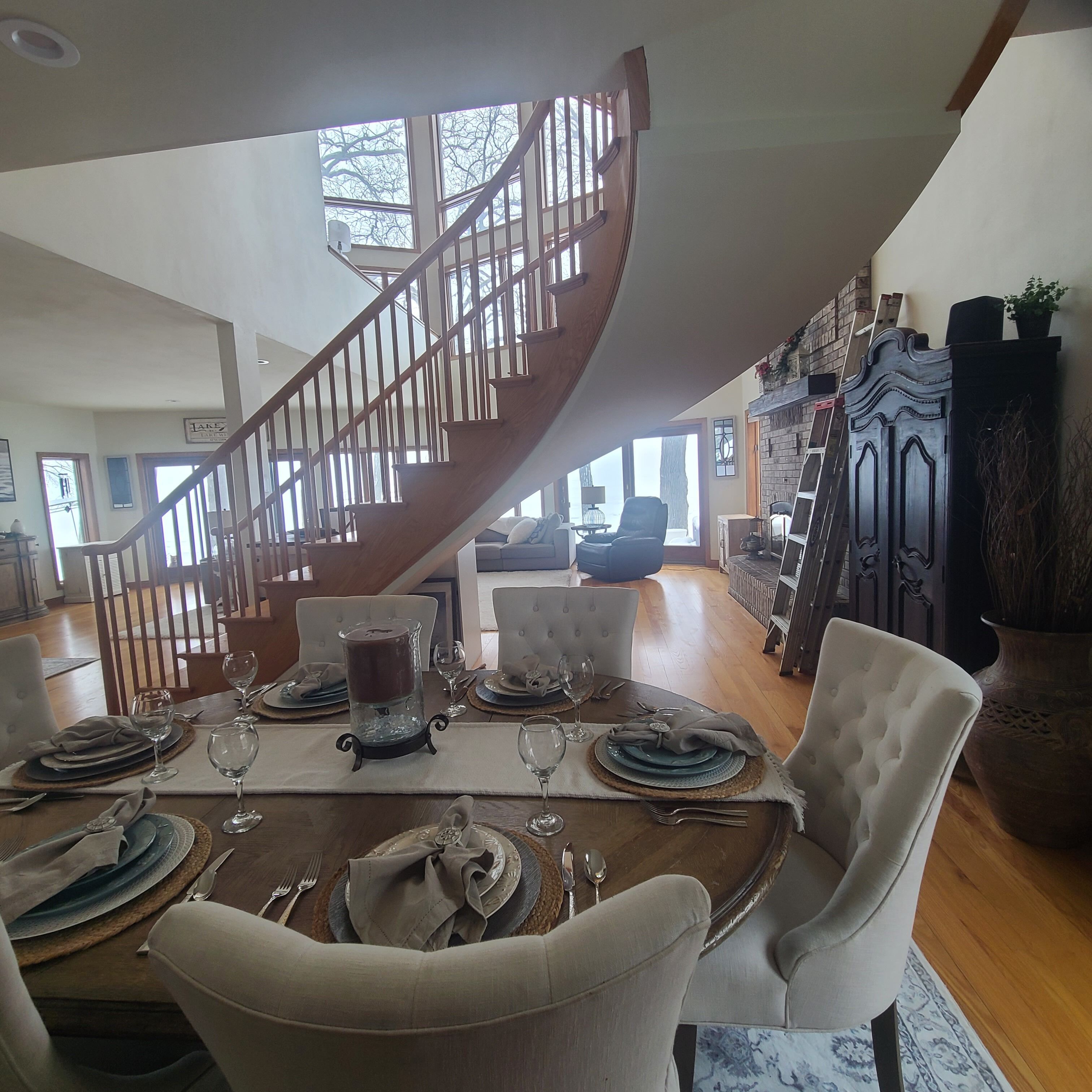 A dining area with a wooden staircase, a fireplace, and a view of the outdoors.