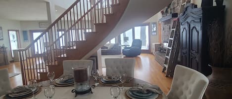A dining area with a wooden staircase, a fireplace, and a view of the outdoors.