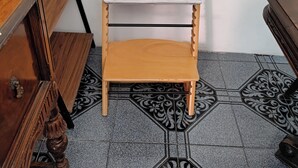 Huoneen nurkka, jossa on puinen tuoli, valkoinen hylly ja kuviollinen lattia.