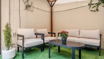 Een patio met een bank, twee stoelen, een kleine ronde tafel en een potplant.