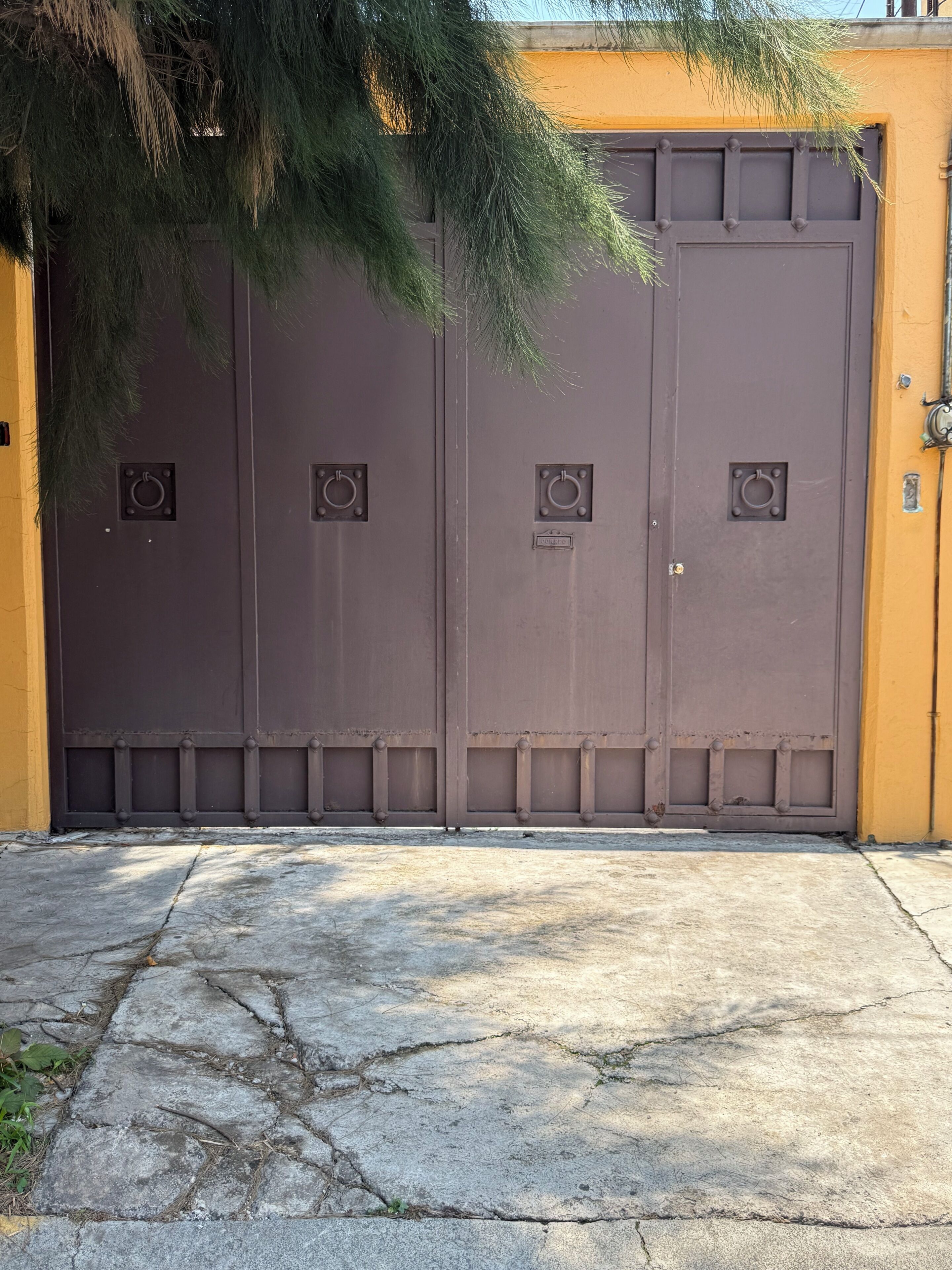 A large, closed metal gate with a circular handle, set against a yellow wall.