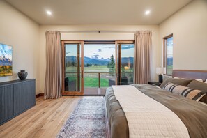 A bedroom with a large bed, a view of a mountainous landscape through a sliding door, and a painting on the wall. - Luxury Retreat, Teton Views, Sleeps 16+, Hot Tub, Fire Pit (Tetonia)