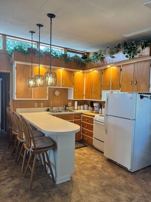 Eine moderne Küche mit Holzschränken, einer zentralen Kücheninsel mit Barhocker, einem Kühlschrank und Pendelleuchten.