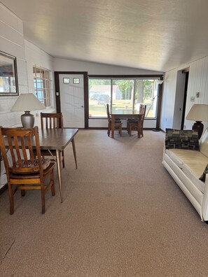A room with a dining table and chairs, a sofa, a lamp, and a door leading to a balcony. - Spacious 4-bedroom house on all sports 8 Pt Lake in wonderful Lake with AC (Lake)