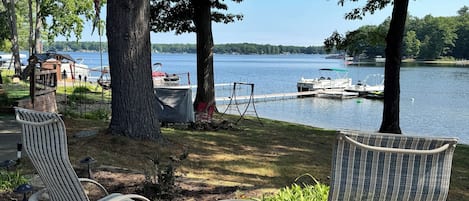 A lakeside patio with two rocking chairs and a small table, overlooking a dock with boats.