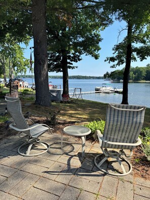 A lakeside patio with two rocking chairs and a small table, overlooking a dock with boats. - Spacious 4-bedroom house on all sports 8 Pt Lake in wonderful Lake with AC (Lake)