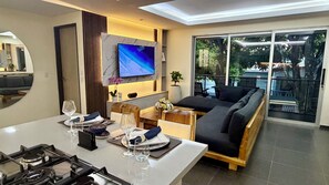 Ein modernes Wohnzimmer mit Essbereich, einem flachbildfernseher an der Wand, einer Couch und einem großen Fenster mit Blick ins Freie.