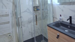 Un baño moderno con cabina de ducha de vidrio, lavabo negro y tocador de madera.