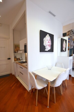 A compact kitchen with white cabinets, a white table, and chairs. There are two black-framed paintings on the wall. - MONACO GOLDEN SQUARE PRESTIGE SUITE (MONACO)