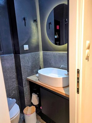 A modern bathroom with a round mirror, a white sink, and a toilet. - Modern Luxury Apartment  Stylish & Cozy Stay (Thessaloniki)