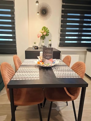 Ein moderner Essbereich mit einem schwarzen Tisch, orangefarbenen Stühlen, einem Willkommensschild und einer Wanddekoration.