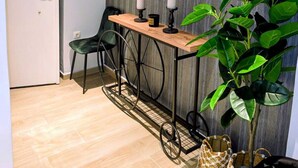 Una habitación con una mesa de madera, dos sillas, una planta en maceta y un panel de control en la pared.