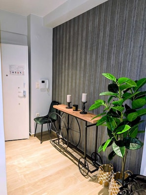 Une pièce comprenant une table en bois, deux chaises, une plante en pot et un panneau de commande fixé au mur.