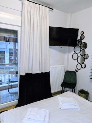Ein Hotelzimmer mit einem Bett, einem Fernseher, einem Sessel, einer Topfpflanze und einem Vorhangfenster.