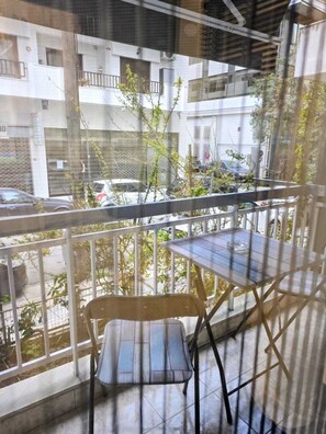 A balcony with a table and chair, overlooking a street with parked cars and buildings. - Modern Luxury Apartment  Stylish & Cozy Stay (Thessaloniki)