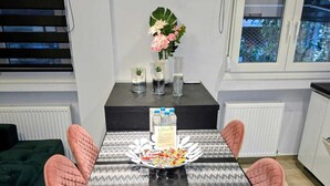 Un comedor con una mesa negra, sillas rosas, un jarrón de flores y un reloj en la pared.