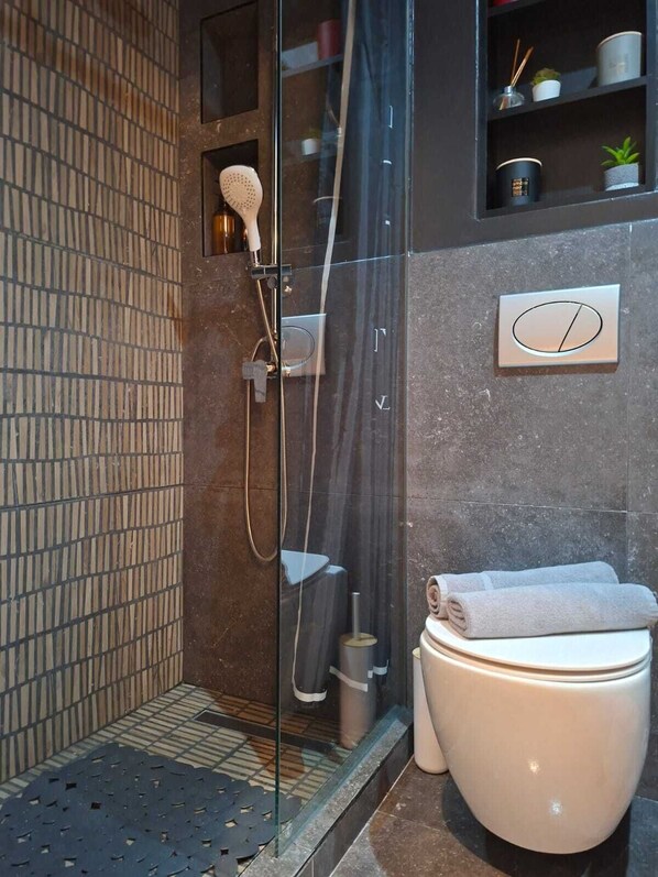 Ein modernes Badezimmer mit Duschkabine aus Glas, Toilette und einer kleinen Ablage für Toilettenartikel.
