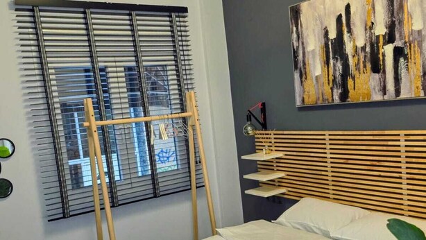 Un dormitorio moderno con cama, escalera de madera, un cuadro y una ventana con persianas.