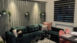 Una sala de estar moderna con un sofá modular, plantas colgantes, una lámpara de techo redonda y un ventanal con persianas.