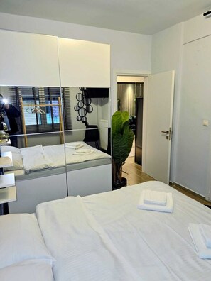 A modern hotel room with a large mirror, a bed with neatly folded white linens, a potted plant, and a view of the hallway. - Modern Luxury Apartment  Stylish & Cozy Stay (Thessaloniki)