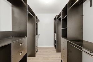 Un vestidor estrecho con estantes y cajones de madera oscura, suelo de madera clara y paredes blancas.