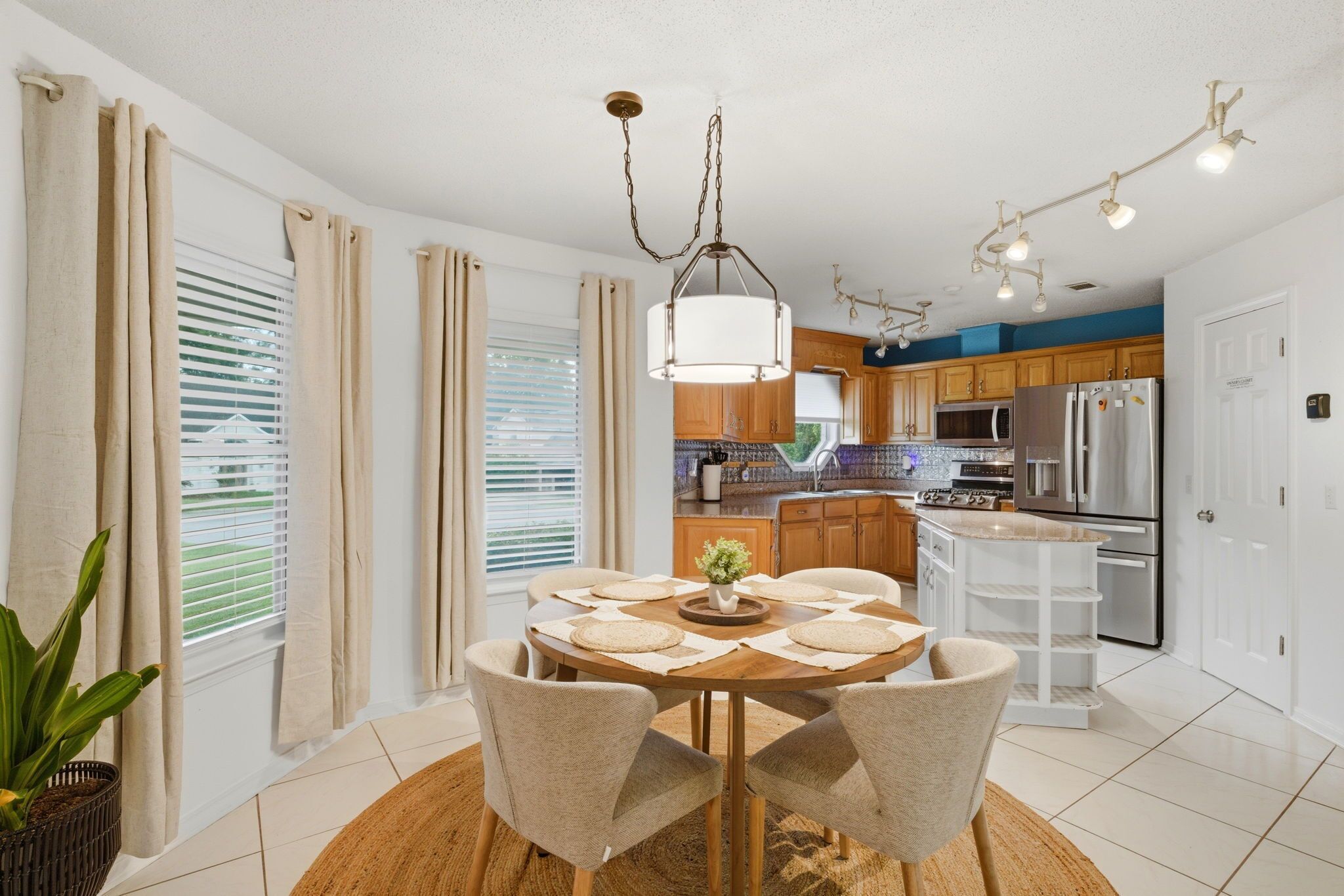 A modern kitchen with a dining area, featuring a round table with chairs, a hanging light fixture, and a refrigerator.