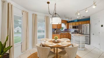 A modern kitchen with a dining area, featuring a round table with chairs, a hanging light fixture, and a refrigerator.