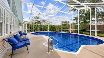 Una piscina techada con agua azul, una escalera y sillas azules.