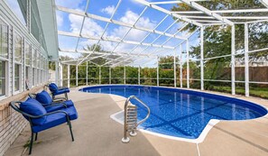 A covered swimming pool with blue water, a ladder, and blue chairs.