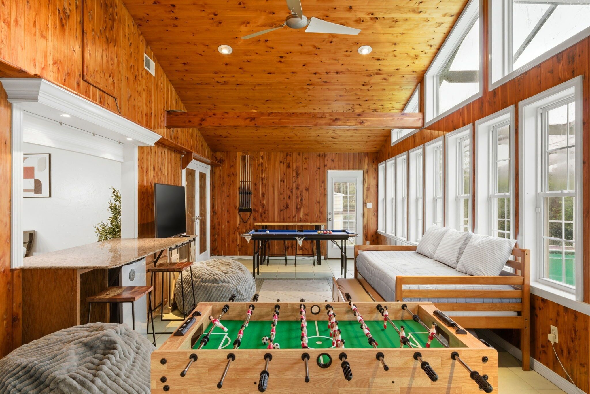 Una habitación acogedora con paredes de madera, una mesa de fútbol de mesa, un sofá y un televisor.