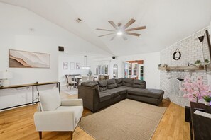 A modern living room with a sectional sofa, a white armchair, a wooden coffee table, and a fireplace with a brick wall.
